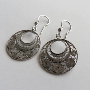 Puede incluir: Un par de pendientes de filigrana de plata con un dise&ntilde;o circular. Los pendientes est&aacute;n hechos de alambre delicado que se teje en un patr&oacute;n intrincado.