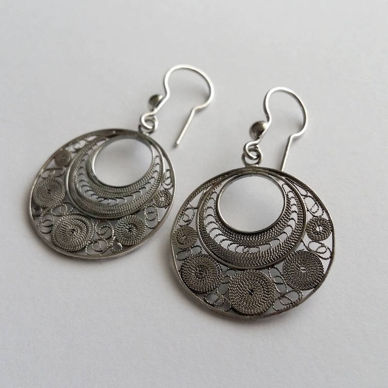 Puede incluir: Un par de pendientes de filigrana de plata con un dise&ntilde;o circular. Los pendientes est&aacute;n hechos de alambre delicado que se teje en un patr&oacute;n intrincado.