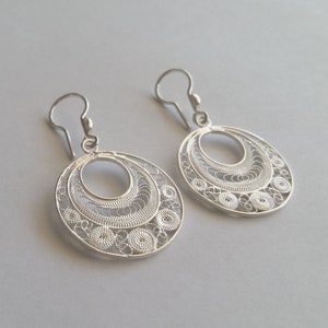Puede incluir: Un par de pendientes de filigrana de plata con un dise&ntilde;o delicado e intrincado. Los pendientes son de forma ovalada y tienen una abertura circular en el centro.