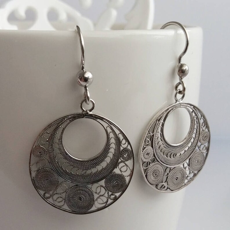 Puede incluir: Un par de pendientes de filigrana de plata con un dise&ntilde;o circular. Los pendientes est&aacute;n hechos de un delicado e intrincado trabajo de alambre y tienen una forma de gota colgante.