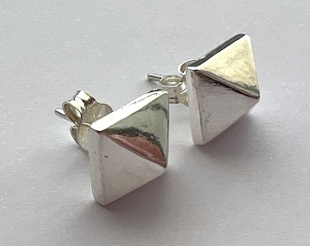 May include: A pair of silver pyramid shaped stud earrings. The earrings are made of a smooth, shiny metal.