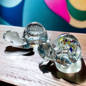 Puede incluir: Dos figuritas de tortuga de vidrio. Una es transparente con burbujas de aire y la otra tiene piezas de vidrio de colores en su interior.