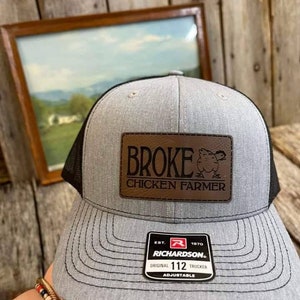 May include: Gray and black trucker hat with a brown leather patch that says "Broke Chicken Farmer". The hat also has a red and black label that says "Richardson 112 Original Trucker Adjustable".