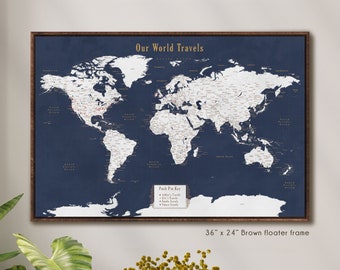 May include: A navy blue world map with white country borders and city names. The map is framed in a brown floater frame and has a push pin key with the text "Our World Travels". The map is 36 inches by 24 inches.