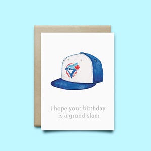 Peut inclure: Carte de vœux avec une illustration à l'aquarelle d'une casquette de baseball bleue et blanche avec un logo d'équipe. La carte contient le texte "i hope your birthday is a grand slam" sur fond blanc, avec une enveloppe beige.