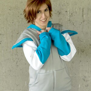 May include: A person wearing a gray zip-up hoodie with white and turquoise accents. The hoodie has a hood and two pockets. The person is wearing blue jeans.