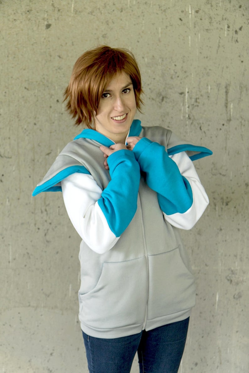 May include: A person wearing a gray zip-up hoodie with white and turquoise accents. The hoodie has a hood and two pockets. The person is wearing blue jeans.