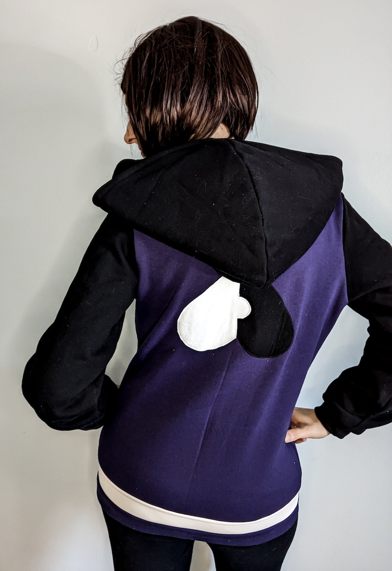 May include: A purple hoodie with a black and white heart design on the back. The hoodie has a black hood and white trim around the bottom.