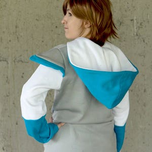 May include: A gray hooded sweatshirt with white and blue accents. The sweatshirt has a white hood with a blue lining and a white inner lining. The sleeves are white with blue cuffs and the shoulders have a gray patch.