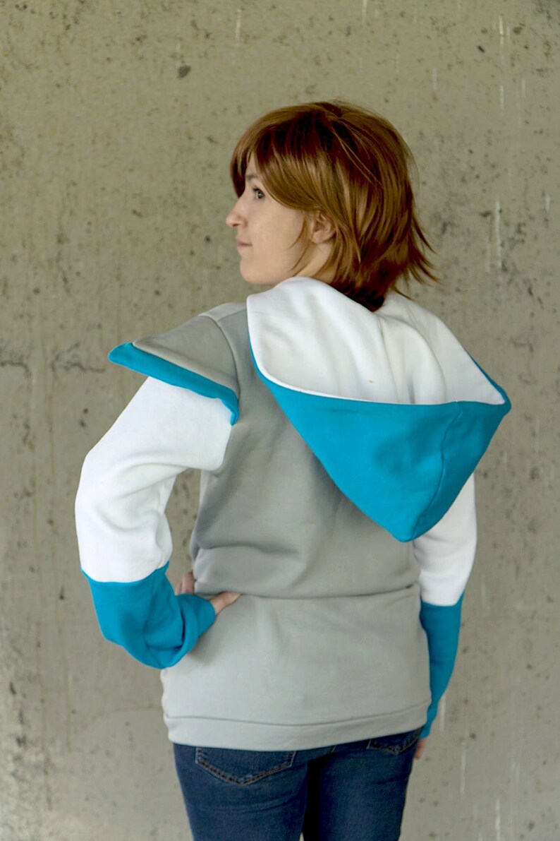 May include: A gray hooded sweatshirt with white and blue accents. The sweatshirt has a white hood with a blue lining and a white inner lining. The sleeves are white with blue cuffs and the shoulders have a gray patch.