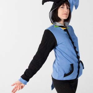 May include: A blue and black hooded zip-up sweatshirt with a unique jester-style hood. The sweatshirt features black sleeves, a blue body, and black trim. The hood has a black and blue design. The model is wearing black pants.