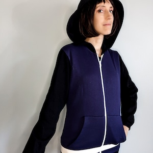 May include: A purple and black zip-up hoodie with a white zipper and white trim around the waist. The hoodie has a black hood and a kangaroo pocket.