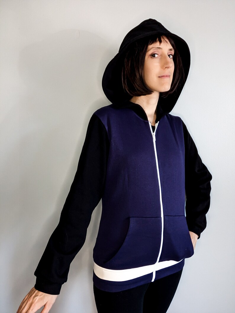 May include: A purple and black zip-up hoodie with a white zipper and white trim around the waist. The hoodie has a black hood and a kangaroo pocket.