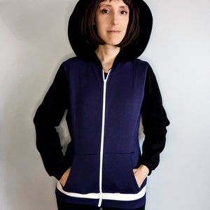 May include: A navy blue zip-up hoodie with black sleeves and a white stripe at the bottom. The hoodie has a black hood and a white zipper.