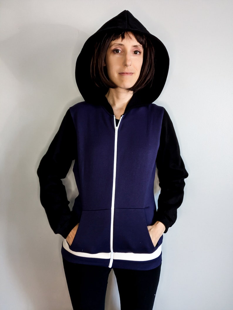 May include: A navy blue zip-up hoodie with black sleeves and a white stripe at the bottom. The hoodie has a black hood and a white zipper.