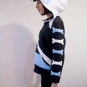 May include: A black and white hoodie with a blue and white bone pattern on the sleeves. The hoodie has a white hood with a blue flame design.