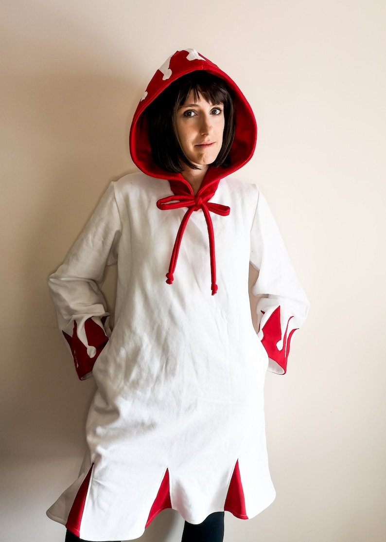 May include: A white hooded robe with red trim and a red bow tie. The hood has white flames on it. The robe has red trim on the sleeves and bottom.