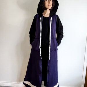 May include: A long purple hooded sweatshirt with white trim and a black zipper. The hood is pulled up and the sweatshirt is unzipped.