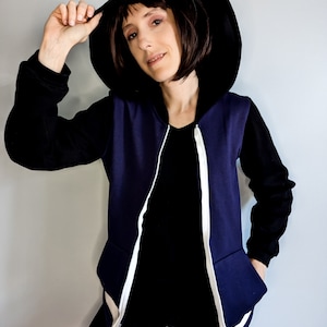 May include: A navy blue zip-up hoodie with black sleeves and white zipper accents. The hoodie has a black hood and a person is wearing it.