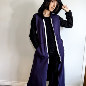 May include: A long, purple hooded sweatshirt with a white zipper and white trim. The hood is black and the sweatshirt has long sleeves.