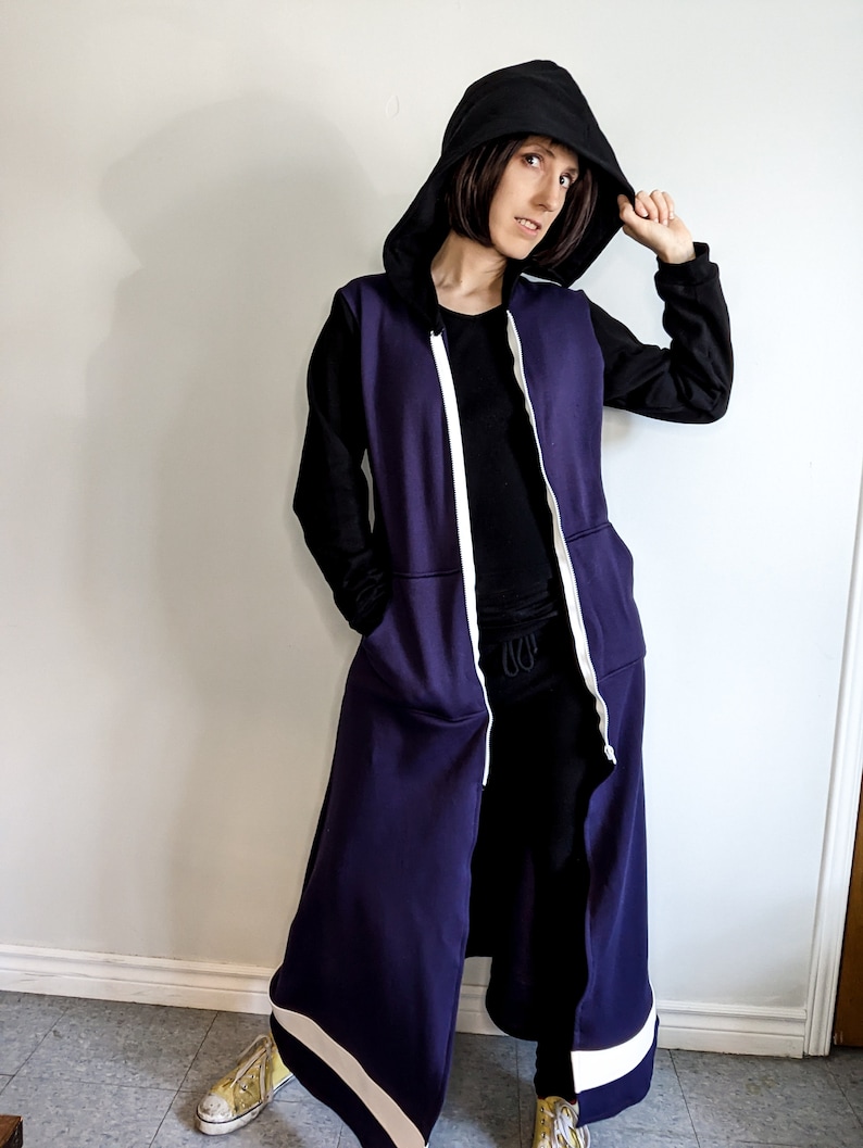 May include: A long, purple hooded sweatshirt with a white zipper and white trim. The hood is black and the sweatshirt has long sleeves.