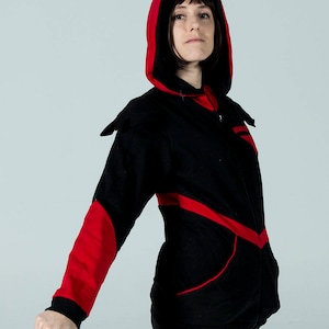 Puede incluir: Una sudadera con capucha negra con detalles rojos. La capucha est&aacute; forrada en rojo y la sudadera tiene ribetes rojos alrededor de los bolsillos y las mangas.