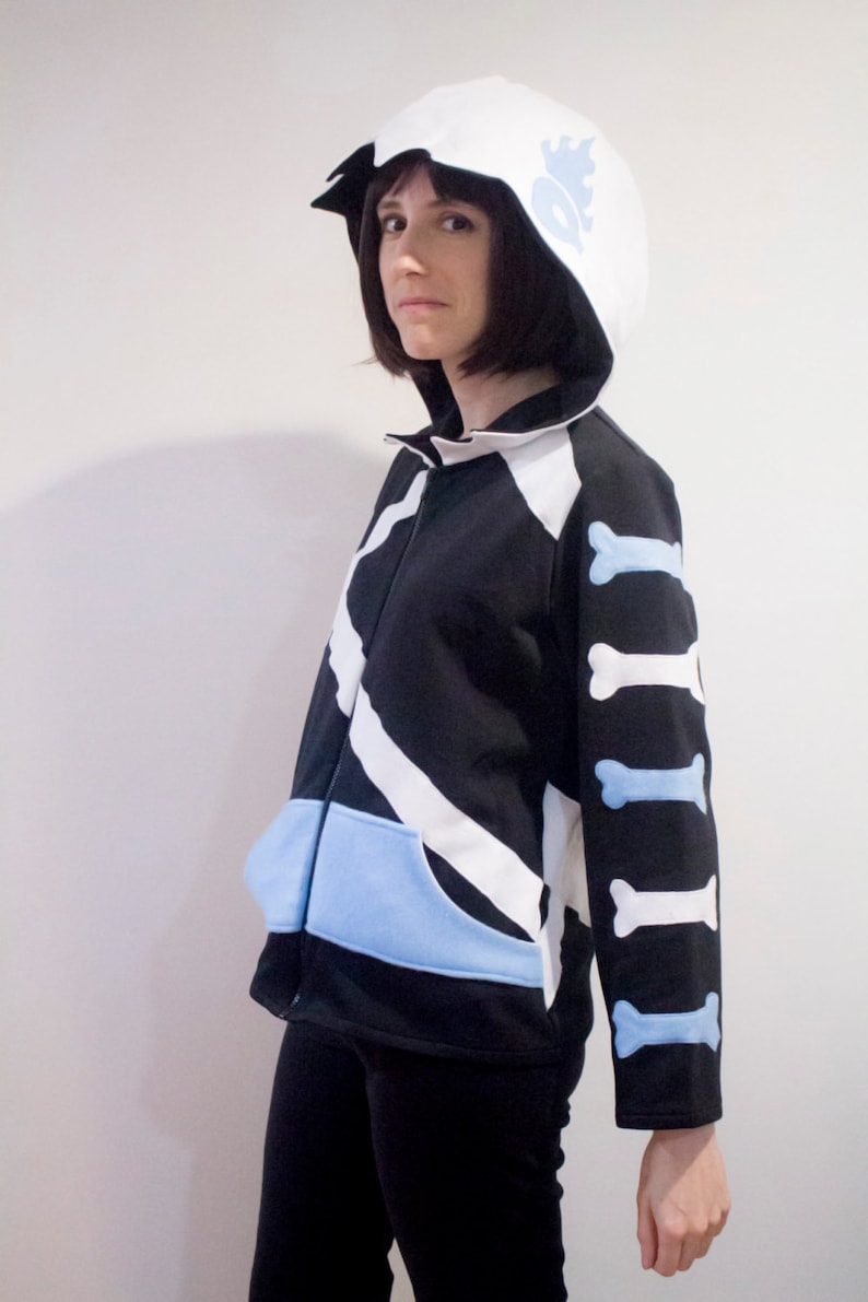 May include: A black and white striped hoodie with a white hood and blue bone accents on the sleeves. The hoodie has a blue pocket on the front.