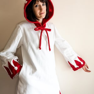 May include: A white hooded robe with red trim and white crown designs on the sleeves and hood. The robe has a tie at the neck.
