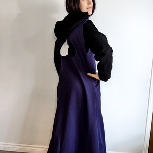 May include: A woman wearing a long, dark purple dress with a white trim at the bottom. The dress has a white heart shape on the back. She is also wearing a black hooded sweatshirt.
