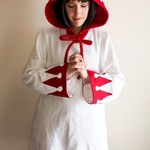 May include: A white hooded robe with red trim and white crown designs. The hood is tied with a red ribbon.