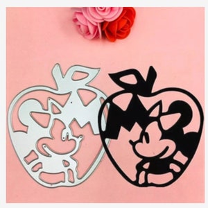 May include: Two metal die-cut stencils in the shape of an apple with a cartoon mouse inside. One stencil is silver and the other is black.