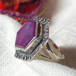 May include: A silver ring with a large, rectangular, deep purple gemstone. The gemstone is set in a decorative, textured silver setting. The ring's band is a simple, polished silver.