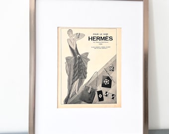 Puede incluir: Una impresión publicitaria vintage enmarcada con una ilustración en blanco y negro de una persona con vestido, un bolso y accesorios. El texto dice POUR LE SOIR HERMÈS 24, Faubourg Saint-Honoré PARIS. Un bolígrafo negro está colocado frente al marco.