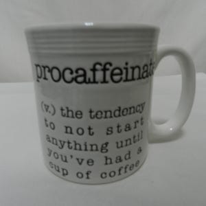 May include: White ceramic coffee mug with the word "procaffeinate" and a definition printed in black. The definition reads: "(v.) the tendency to not start anything until you've had a cup of coffee."