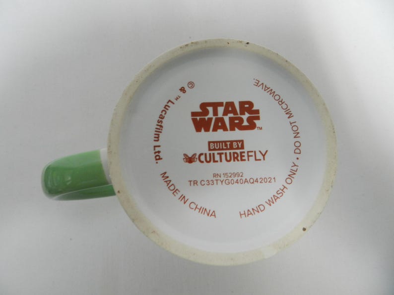 Op de afbeelding: Witte keramische mok met een groene handgreep. De bodem van de mok toont het Star Wars-logo en de tekst "BUILT BY CULTUREFLY". Extra tekst is "ALLEEN HANDWAS. NIET IN DE MAGNETRON."