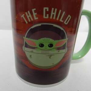Op de afbeelding: Een keramische mok met het personage "The Child" uit de Star Wars-serie. De mok heeft een donkerrode achtergrond met de woorden "THE CHILD" in het wit. De handgreep is lichtgroen en de afbeelding van het personage staat in een lichtgroene drager.