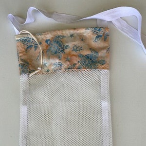 May include: A reusable mesh produce bag with a white drawstring closure and a white strap. The top section features a fabric with a pattern of blue sea turtles, starfish, and coral on a tan background.