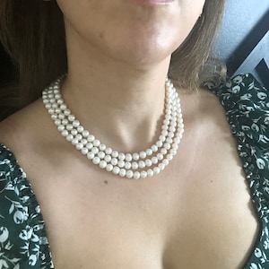 Puede incluir: Una mujer con una blusa verde floral y un collar de perlas de tres hileras.