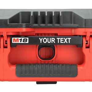 May include: A red and black plastic tool box featuring a black handle with a textured grip. The front panel displays the M18 logo in white and red, followed by the text YOUR TEXT in white lettering on a black horizontal bar.