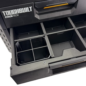 Op de afbeelding: Een zwarte Toughbuilt Stacktech gereedschapskist met een open lade, die een zwarte plastic organizer met meerdere vakken laat zien.