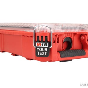 Puede incluir: Una caja de herramientas de plástico rojo con tapa transparente y asa metálica. La caja tiene un agarre de asa negro y una etiqueta que dice "M18 YOUR TEXT". El texto "CASE NOT INCLUDED" está en la parte inferior.