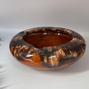 May include: A round, ceramic ashtray with a glossy finish. The ashtray features a brown and black marbled design. The interior is a solid brown color. The ashtray has three small indentations for holding cigarettes.