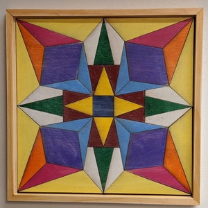 May include: A framed geometric art piece with a starburst design. The artwork features a variety of colors, including yellow, orange, red, purple, blue, green, and white.
