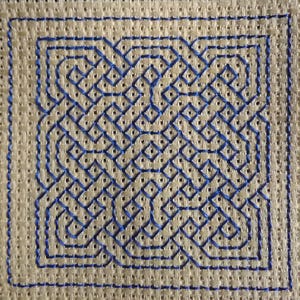 Puede incluir: Un diseño de nudo celta azul bordado sobre un fondo de tela beige.