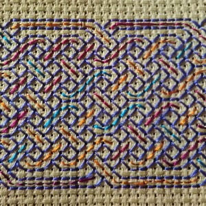 Puede incluir: Un primer plano de un patrón de punto de cruz colorido con un diseño tejido. El patrón presenta una variedad de colores, incluyendo azul, morado, naranja y rojo.