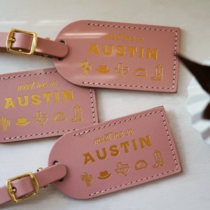 K&ouml;nnte beinhalten: Drei rosafarbene Leder-Gep&auml;ckanh&auml;nger mit goldener Aufschrift "Meet me in Austin". Jeder Anh&auml;nger ist mit einem goldenen Kaktus-, Cowboyhut-, Texasstern-, Taco- und Cowboystiefel-Symbol verziert.