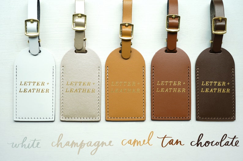 May include: Five leather luggage tags in different colors: white, champagne, camel, tan, and chocolate. Each tag has the text "LETTER + LEATHER" embossed in gold.