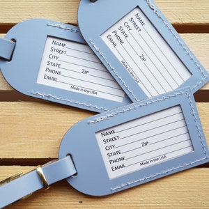 May include: Three blue leather luggage tags with white stitching and a gold metal loop. Each tag has a blank space for writing "Name", "Street", "City", "State", "Zip", "Phone", and "Email". The tags also have the text "Made in the USA".
