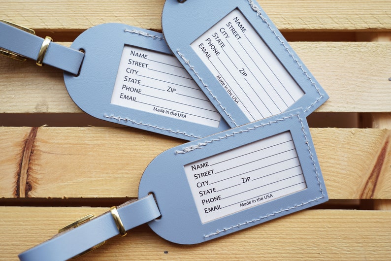 May include: Three blue leather luggage tags with white stitching and a gold metal loop. Each tag has a blank space for writing "Name", "Street", "City", "State", "Zip", "Phone", and "Email". The tags also have the text "Made in the USA".