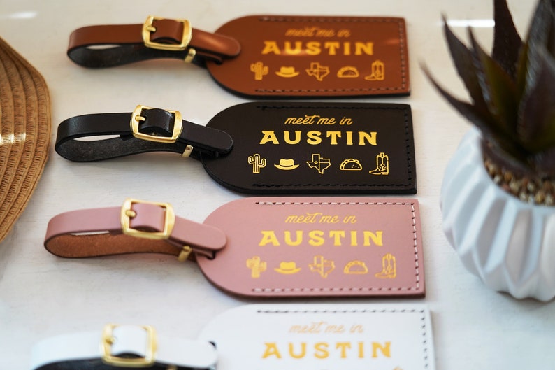 K&ouml;nnte beinhalten: Vier Leder-Gep&auml;ckanh&auml;nger mit goldener Beschriftung und Symbolen. Die Anh&auml;nger zeigen den Text "meet me in AUSTIN" und ein Kaktus, einen Cowboyhut, die Umrisse des Bundesstaates Texas, ein Taco und einen Cowboystiefel. Die Anh&auml;nger sind braun, schwarz, rosa und wei&szlig;.